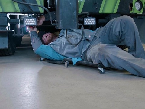 All Fleet Inc technician on a creeper under a truck in a clean shop bay