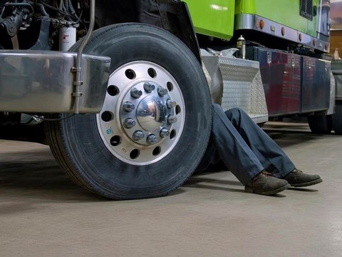 All Fleet Inc technician working under a truck beside a drive wheel on a clean shop floor